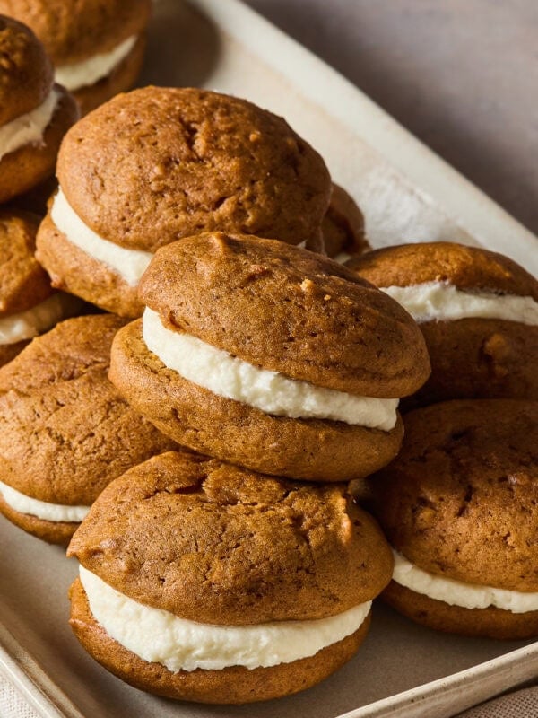 A stack of pumpkin whoopie pies on a baking sheet.