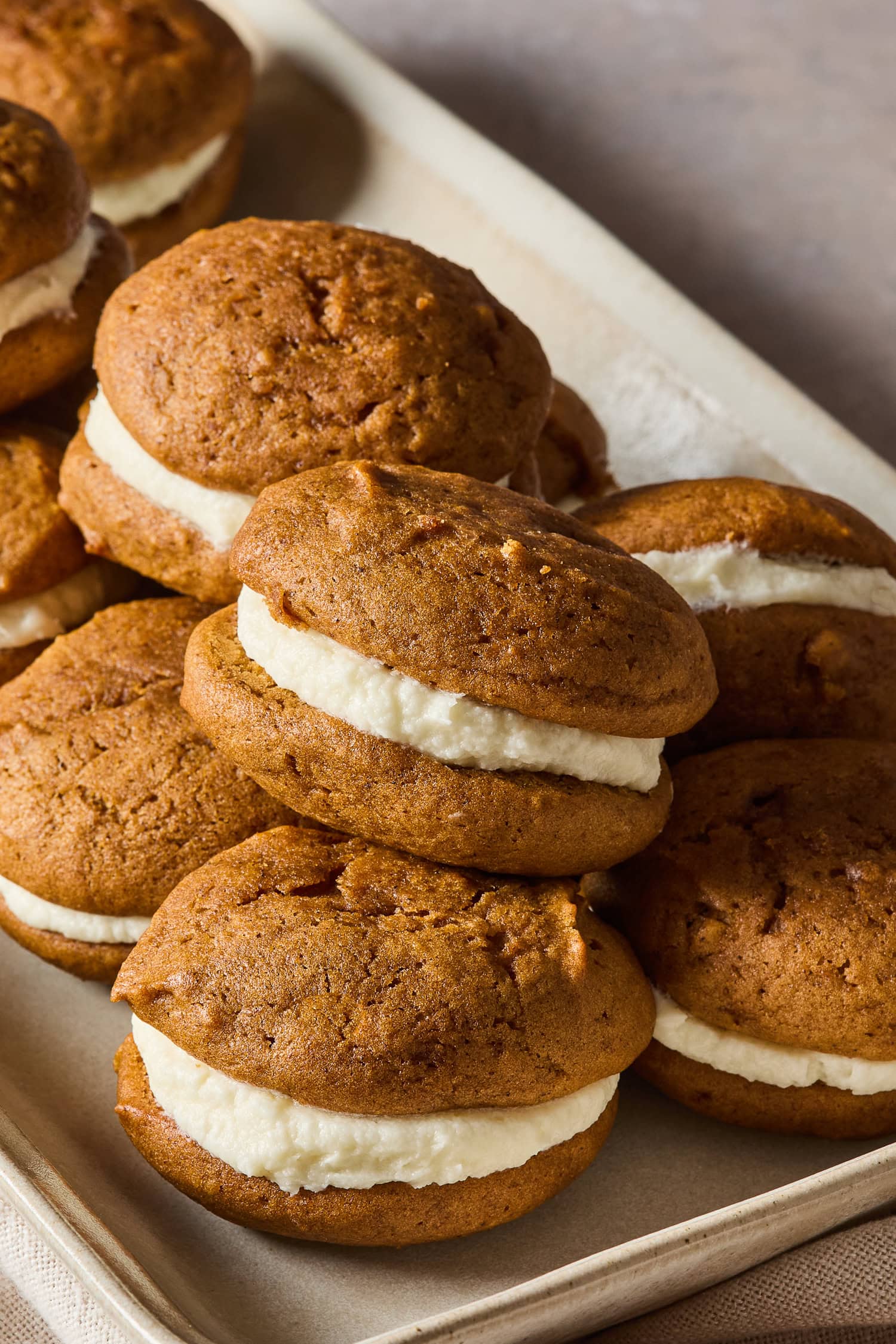 A stack of pumpkin whoopie pies on a baking sheet.