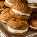 Multiple pumpkin whoopie pies on a baking sheet.