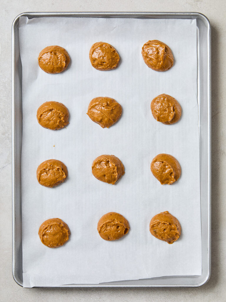 Balls of dough for pumpkin whoopie pies on a baking sheet.