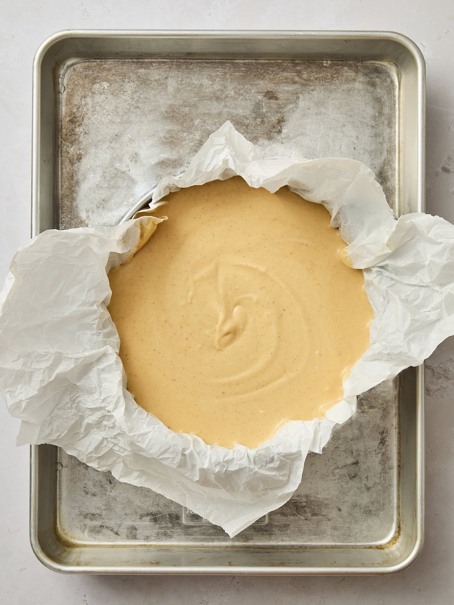 Unbaked Basque cheesecake with parchment on baking sheet.