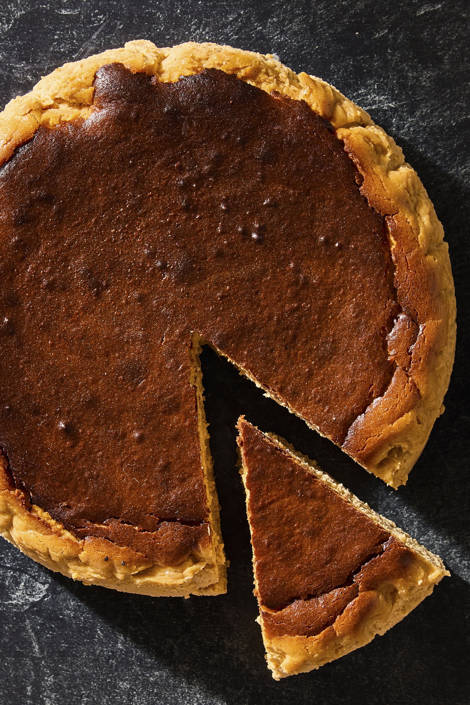 Baked Basque pumpkin cheesecake on dark surface with a single slice cut out.