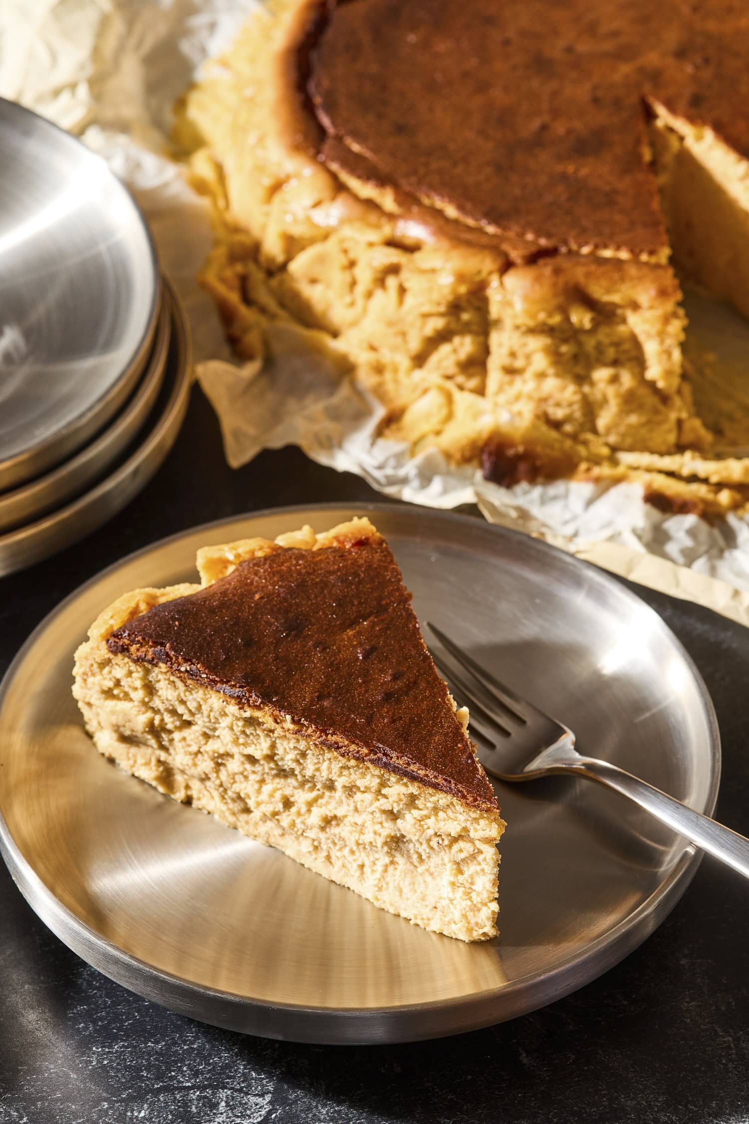 Slice of Basque pumpkin cheesecake on a plate with the rest of the cheesecake in background.