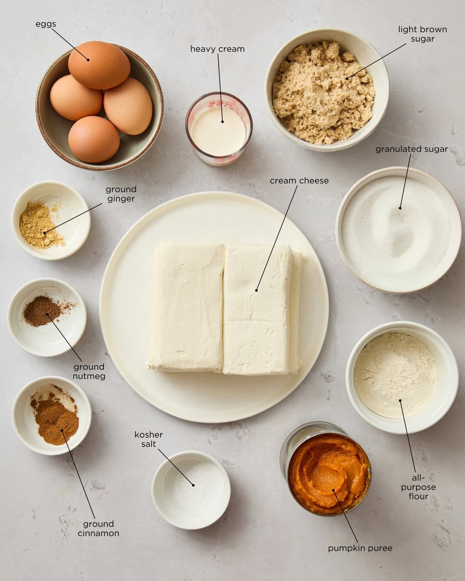 Stone surface with ingredients needed to make Basque pumpkin cheesecake including cream cheese, pumpkin, spices, and more.