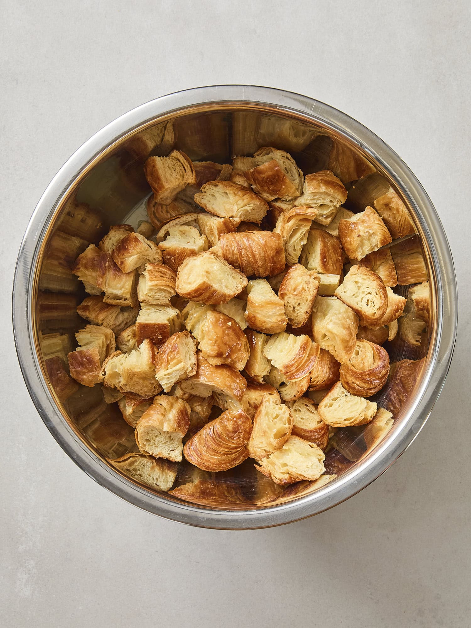 Metal bowl filled with toasted croissant pieces torn into cubes.