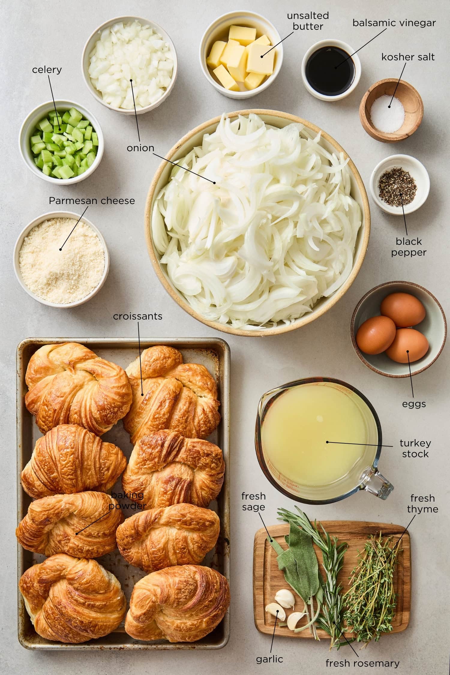 Concrete surface with ingredients needed for croissant stuffing including croissants, Parmesan cheese, onions, and aromatics.