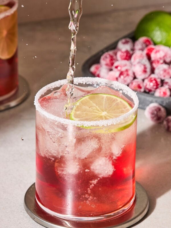 Liquid pouring into a glass filled with cranberry margarita with ice inside.