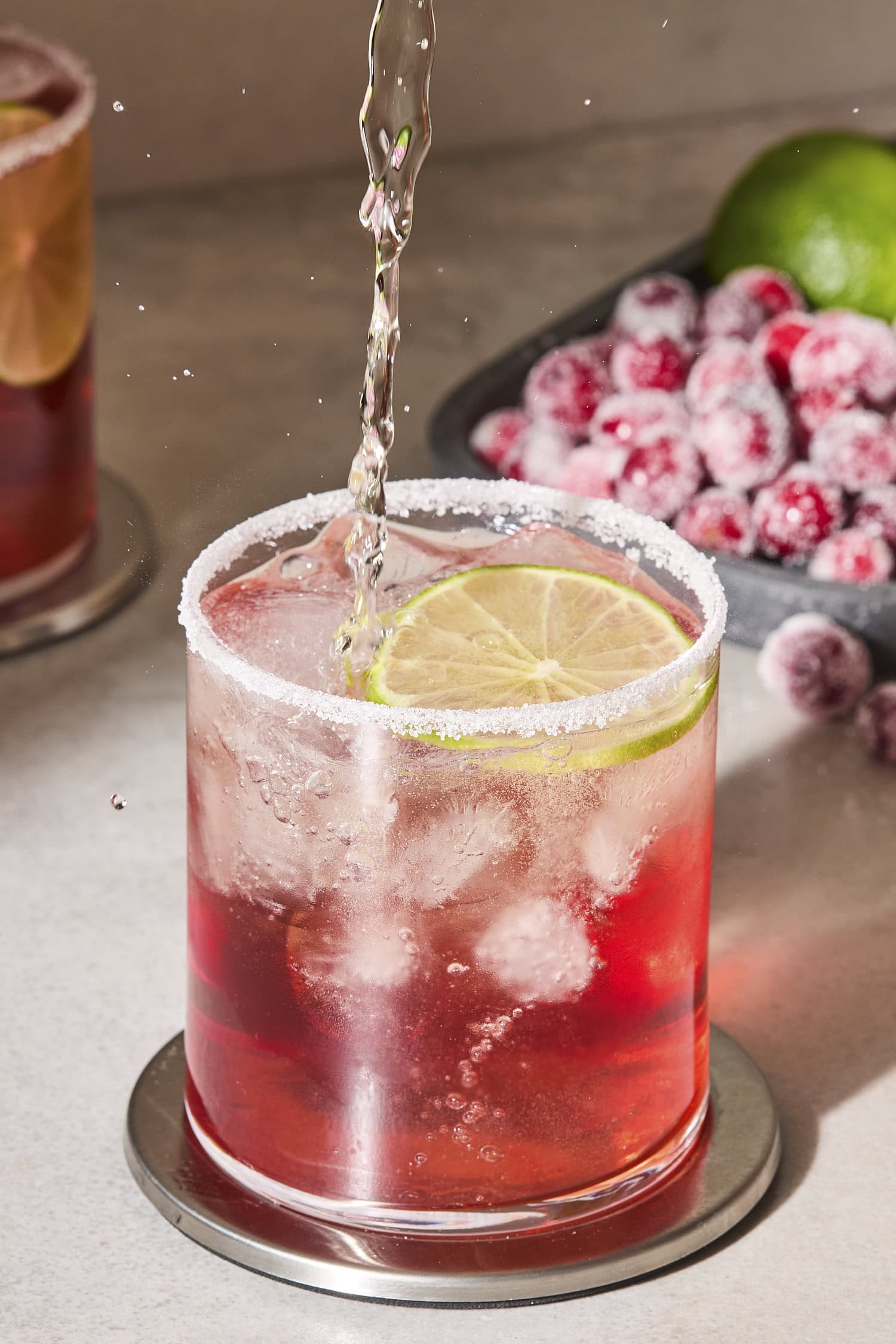 Liquid pouring into a glass filled with cranberry margarita with ice inside.