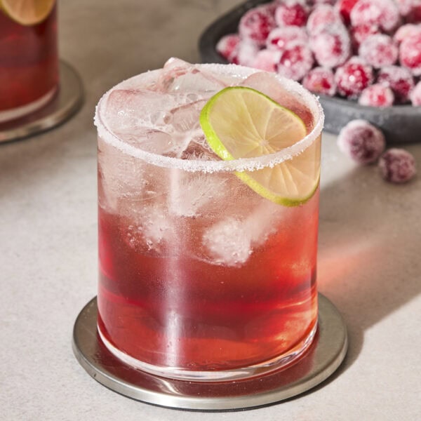 Glass with salted rim and lime wedge filled with a cranberry margarita.