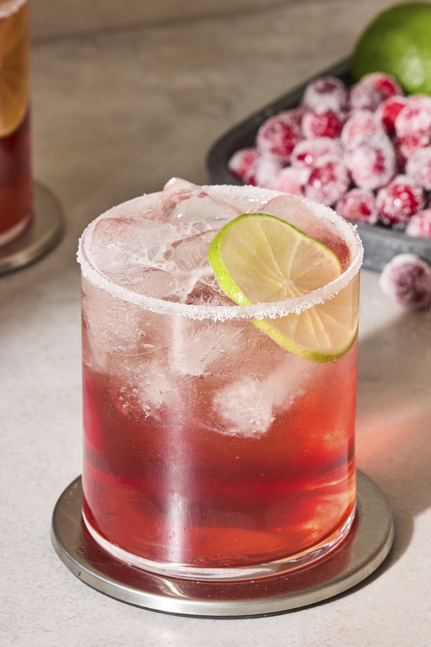 Glass filled with ice and cranberry margarita with a lime wedge.