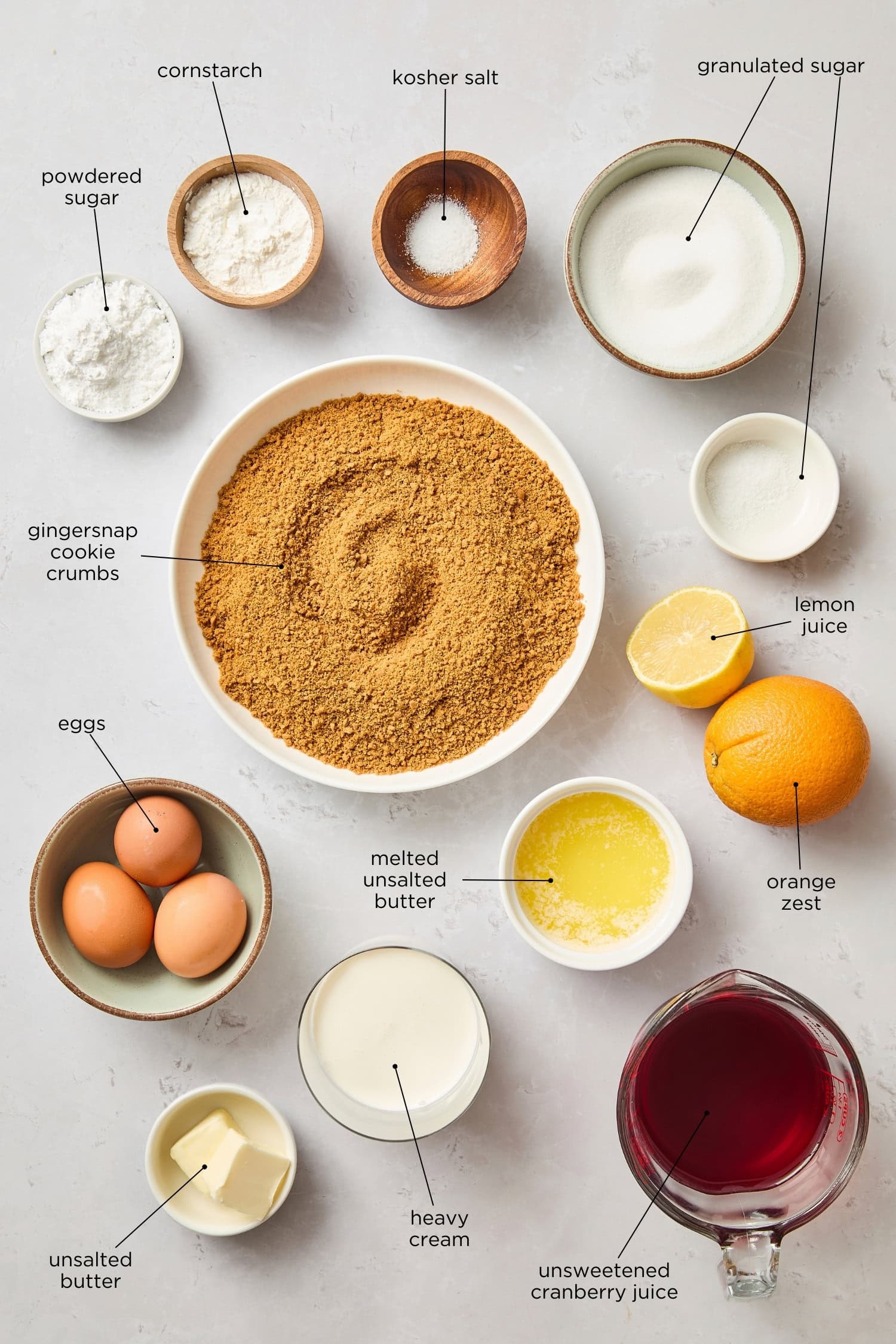 Surface filled with ingredients for a cranberry tart including juice, eggs, gingersnap cookies, eggs, and more.