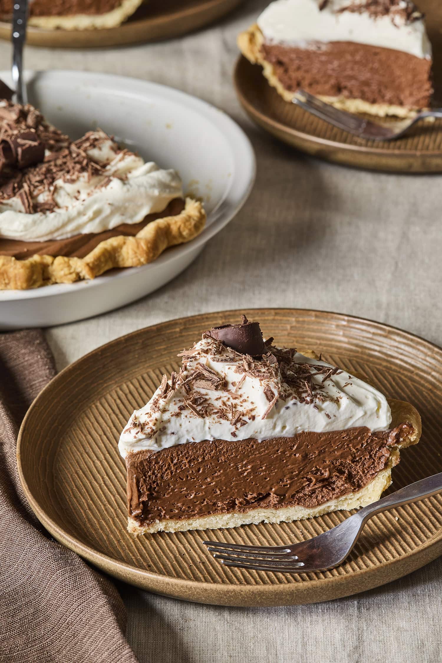 Slice of French silk pie on a brown plate taken from a pie dish in the background.