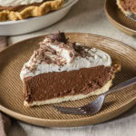 Slice of chocolate French silk pie with whipped cream on top all on a brown plate.