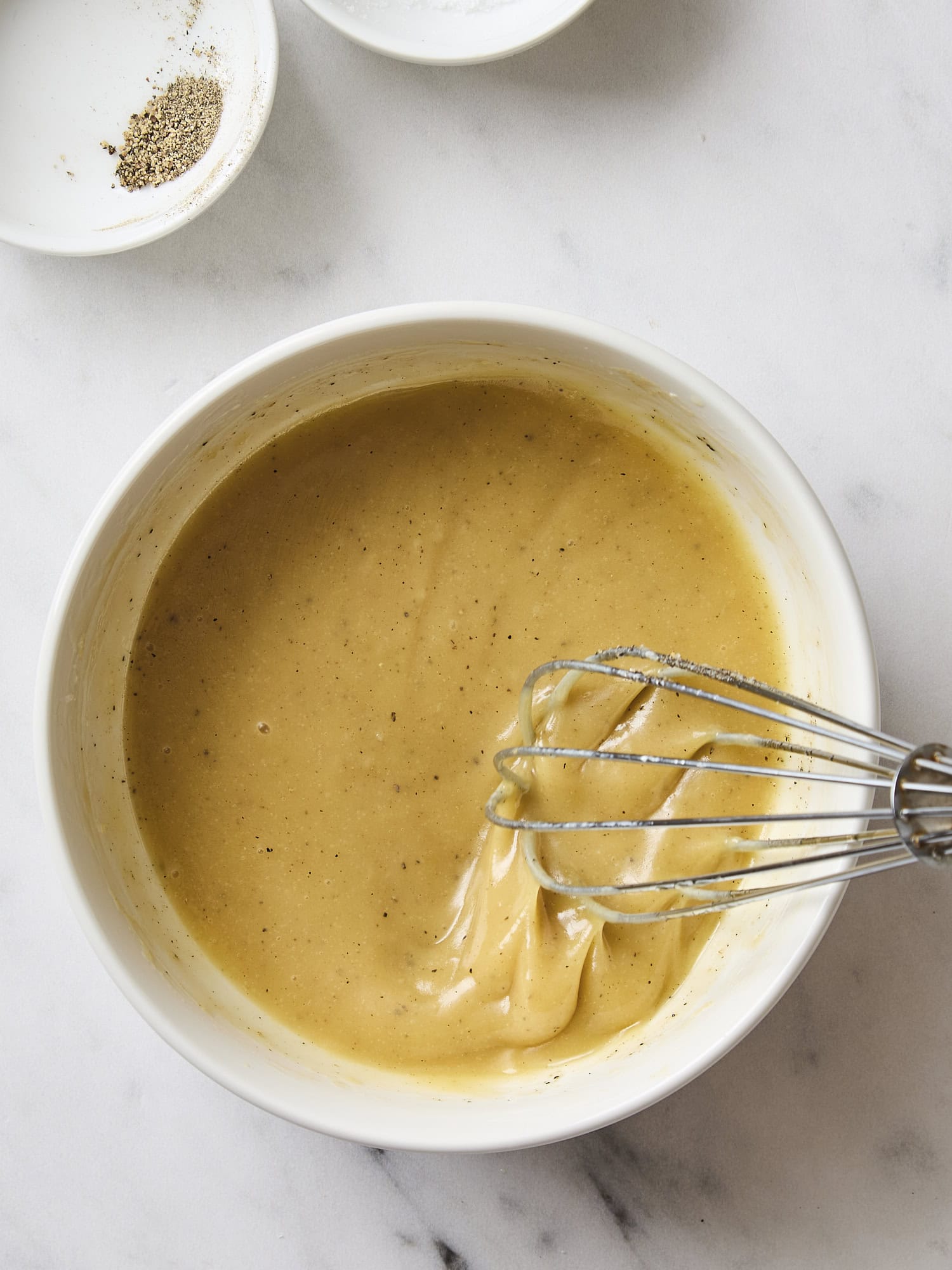 White bowl with whisk mixing together honey Dijon vinaigrette dressing.