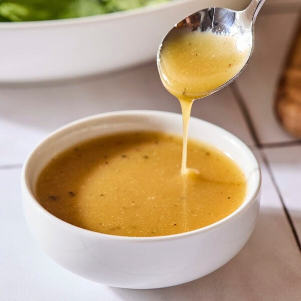 White bowl filled with honey Dijon vinaigrette dressing with a spoon drizzling some.