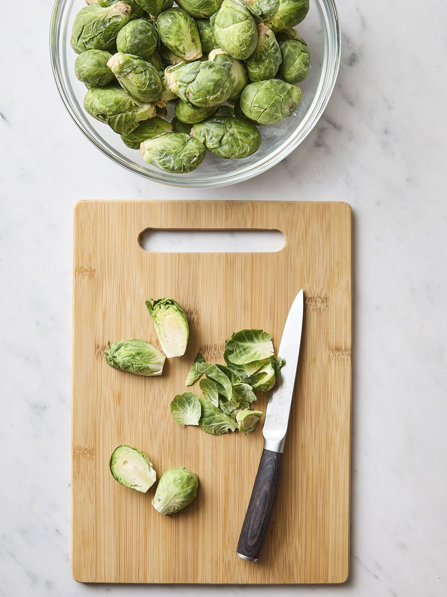 Cutting board with Brussels sprouts and a knife cutting them in half.