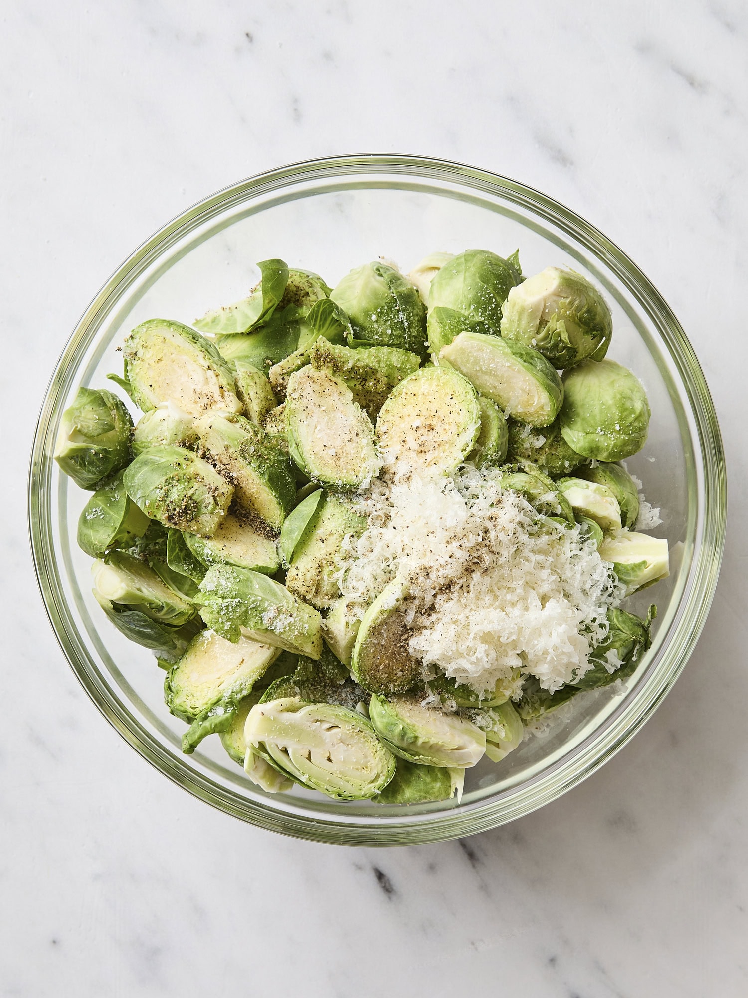 Glass bowl with Parmesan cheese and other toppings being mixed with Brussels sprouts.