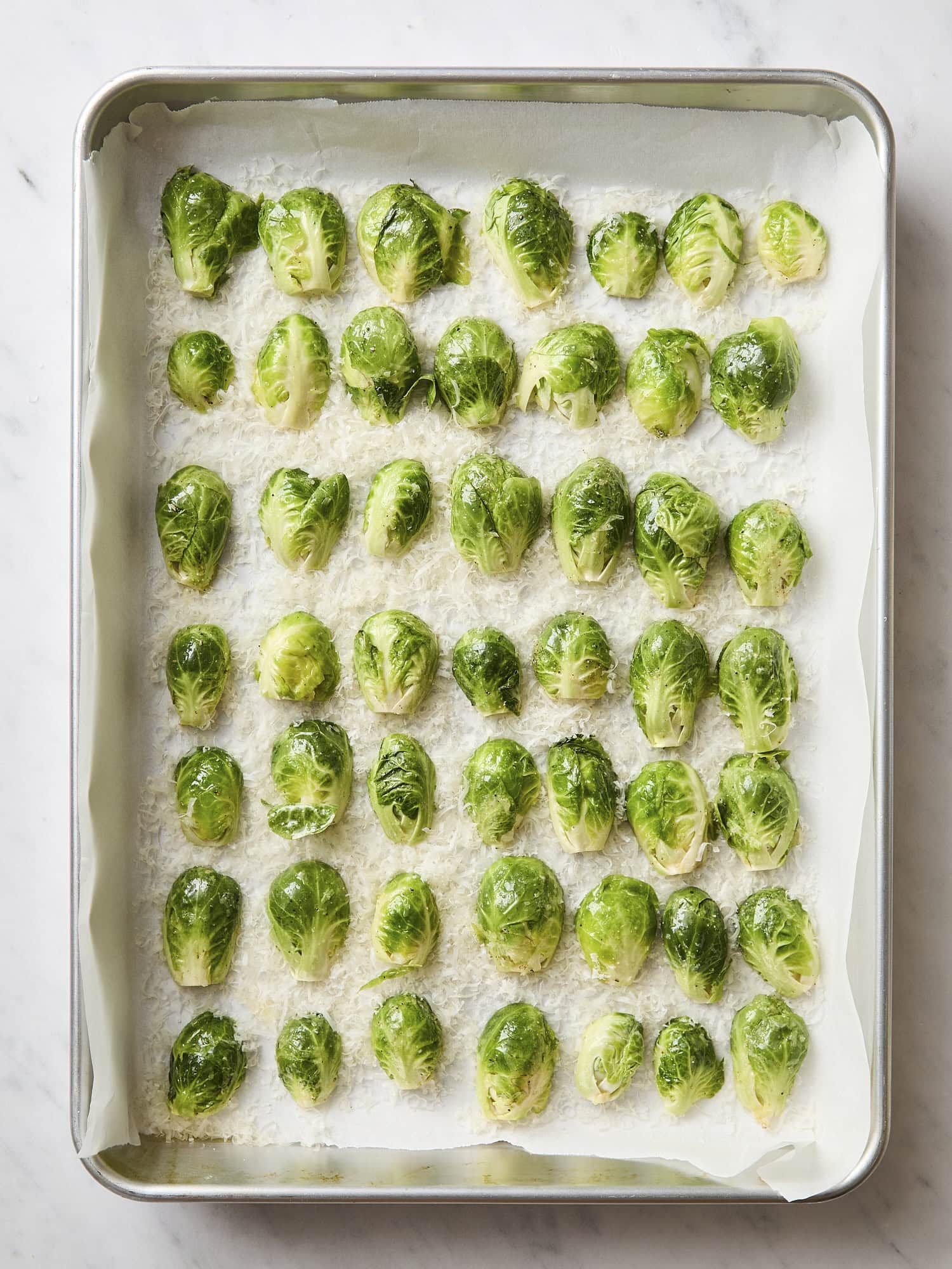 Sheet pan with Brussels sprouts sliced in half laid in Parmesan cheese.
