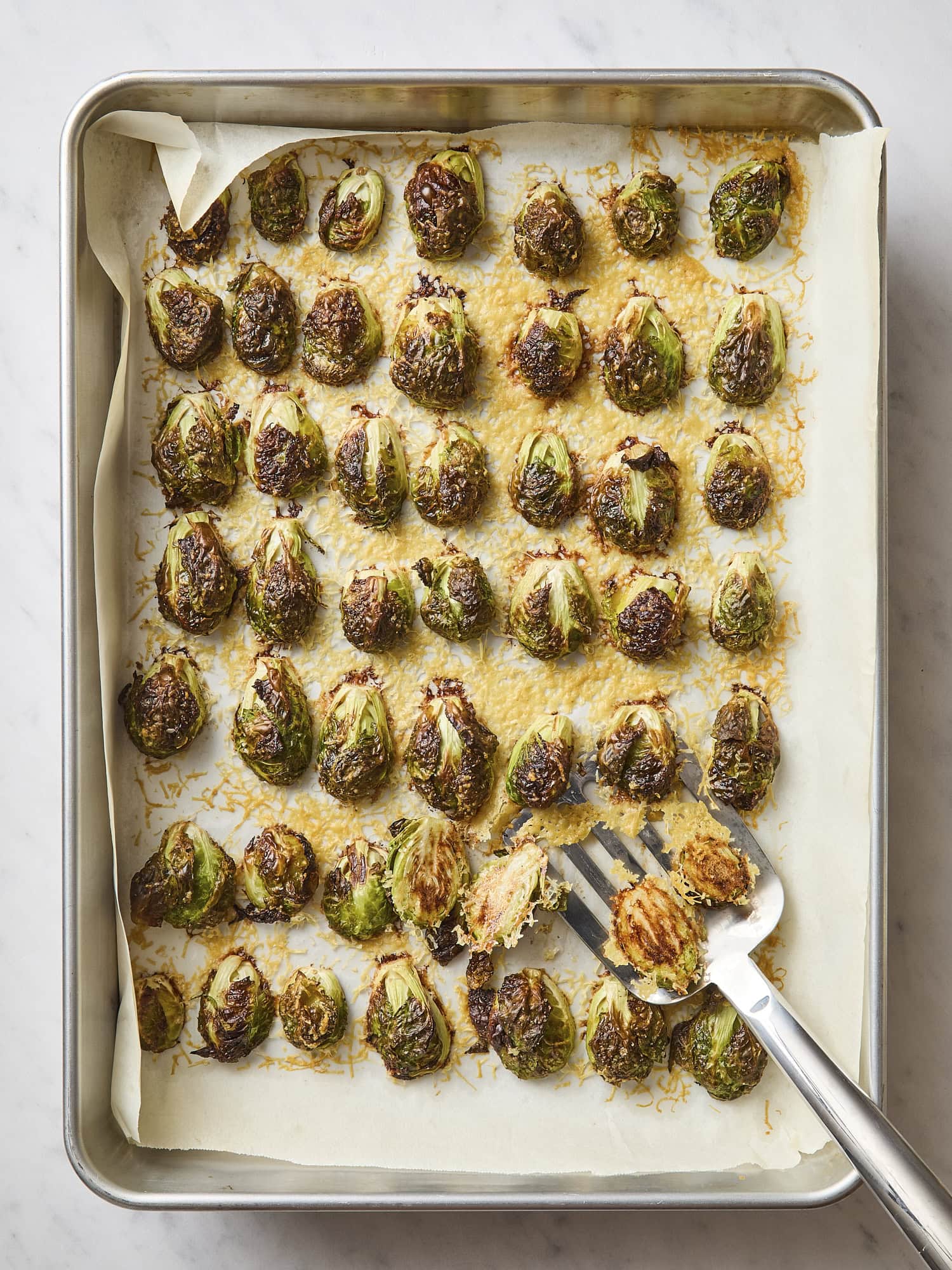 Sheet pan with roasted Parmesan roasted Brussels sprouts with spatula scooping them up.