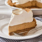 Slice of pumpkin pudding pie with a tall meringue topping with fork on plate.