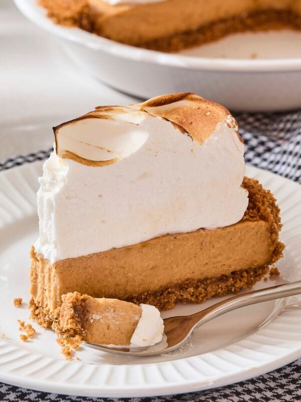 Slice of pumpkin pudding pie with meringue topping with a fork removing a piece.