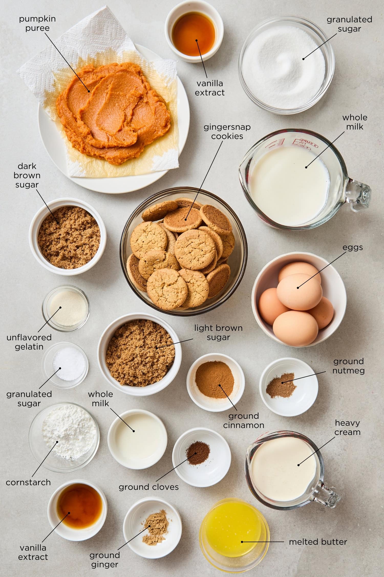 Concrete surface with ingredients for pumpkin pudding pie including gingersnap cookies, eggs, flour, sugar, spices, and more.