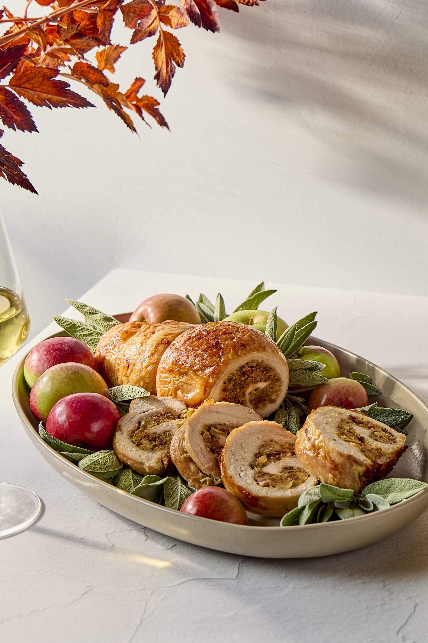 White table with serving of turkey roulade with apple and sage with red leaves.