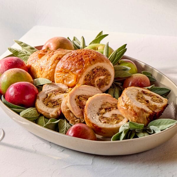 White table with serving platter filled with turkey roulade with slices arranged in front.