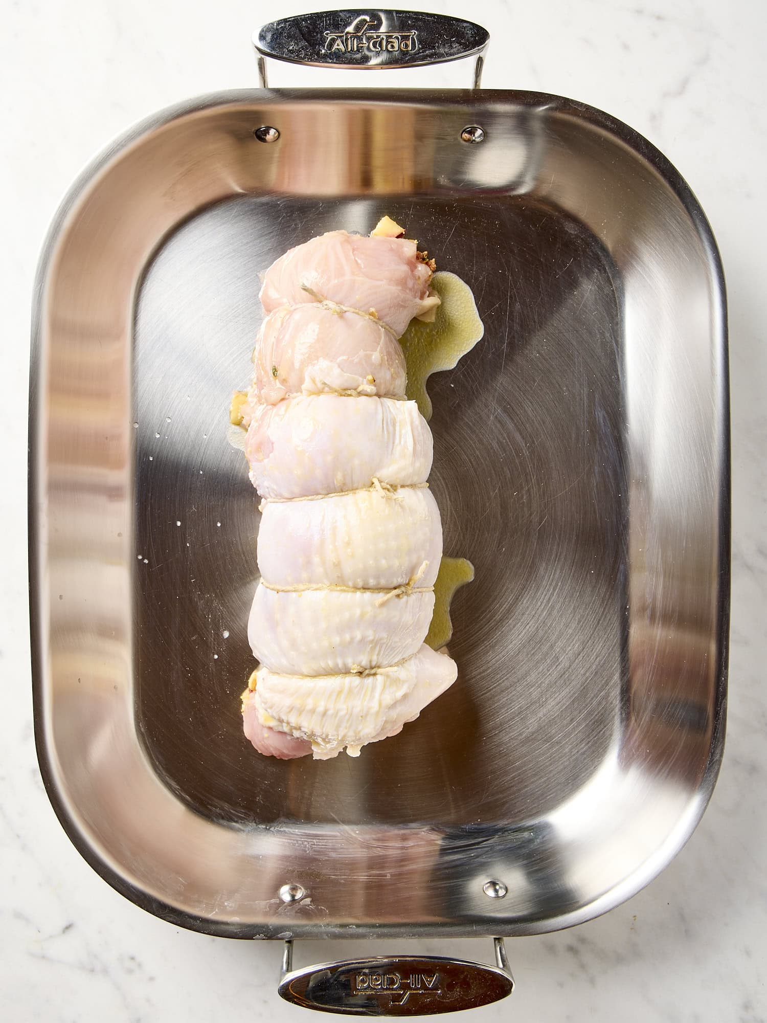 Roasting pan with turkey roulade tied up with twine before being roasted.