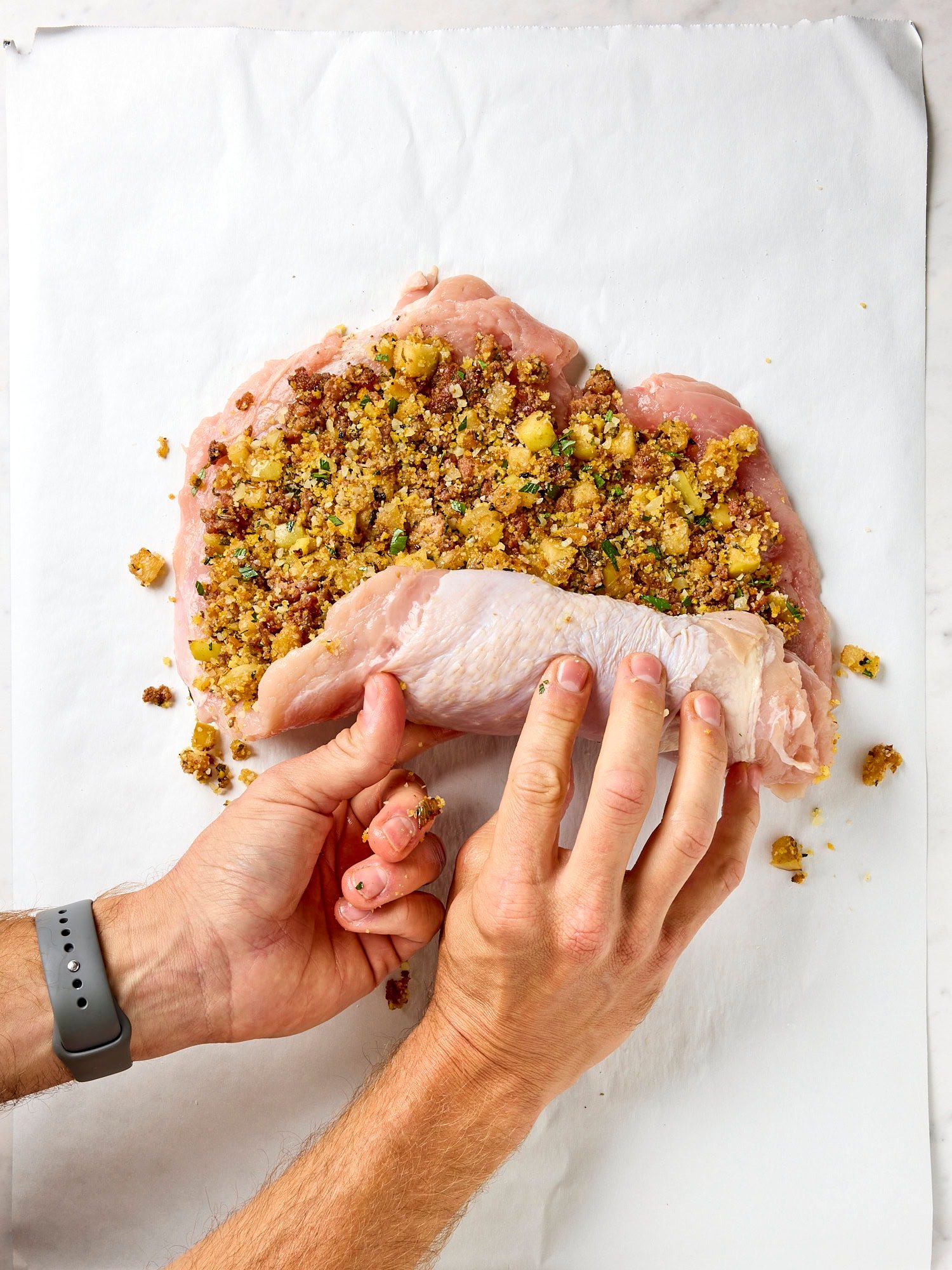 Two hands rolling up a turkey breast with filling inside.