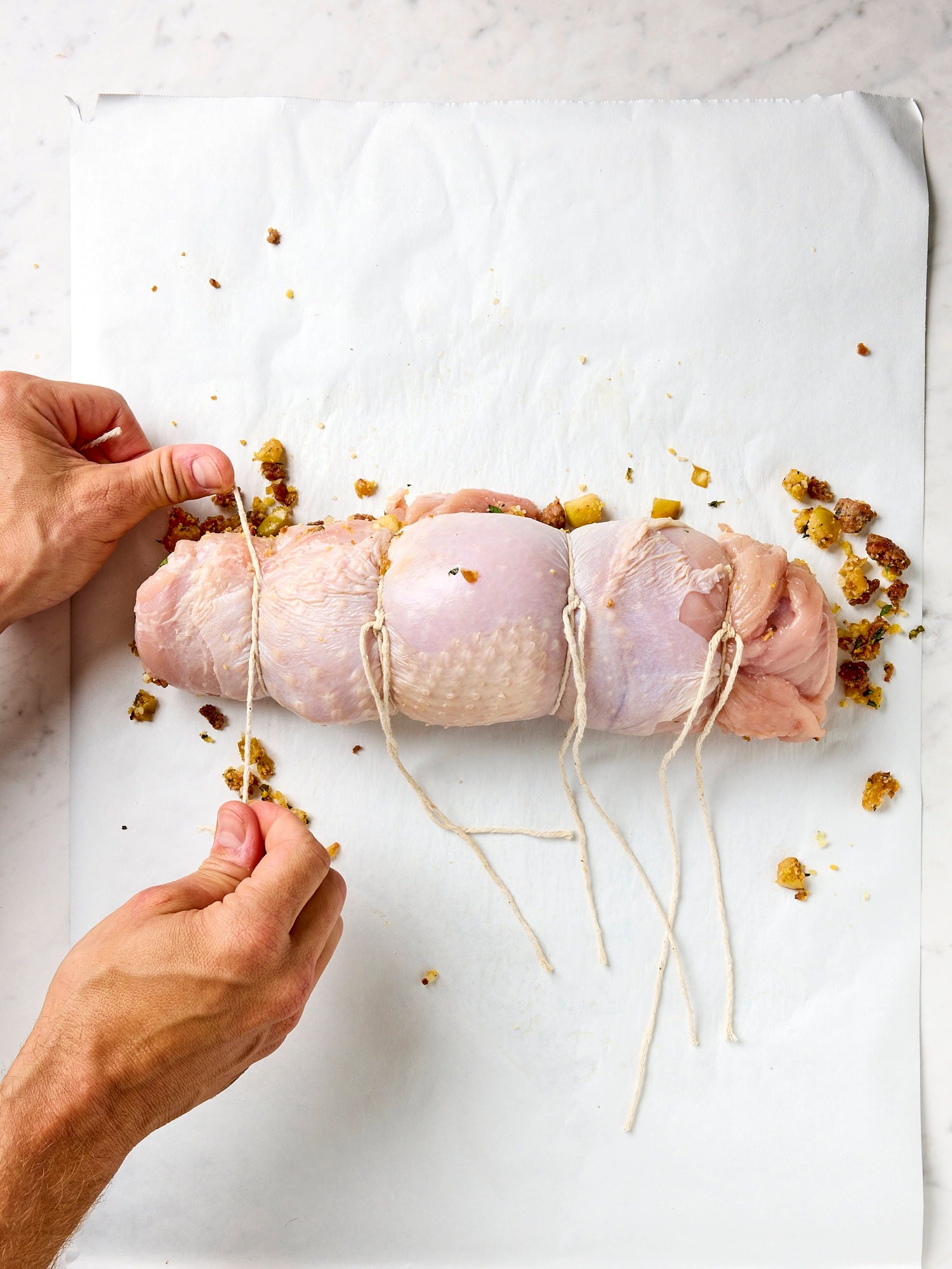 Hands tying twine on a turkey breast with filling inside.