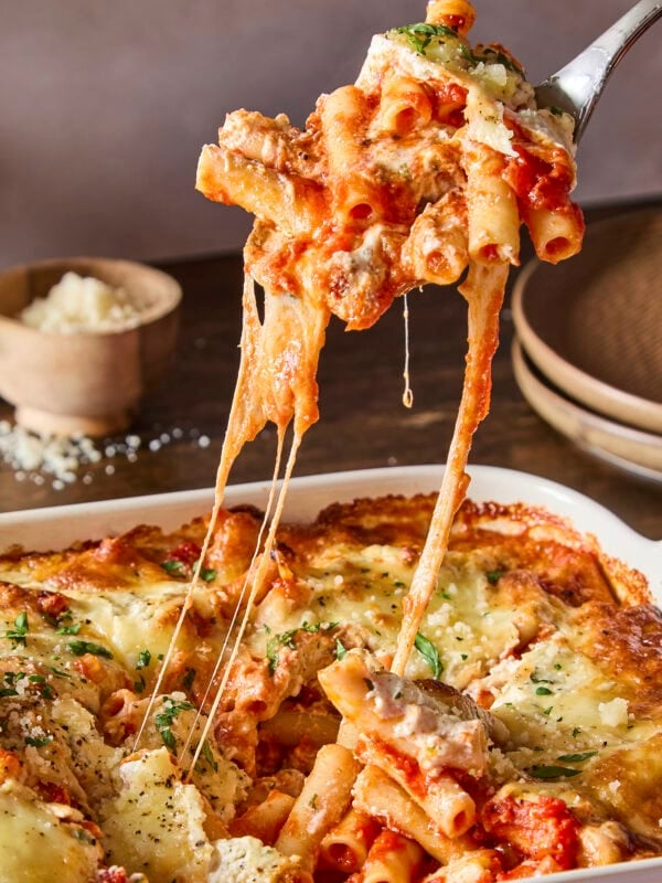Serving of baked ziti being pulled from a casserole dish with a cheese pull.