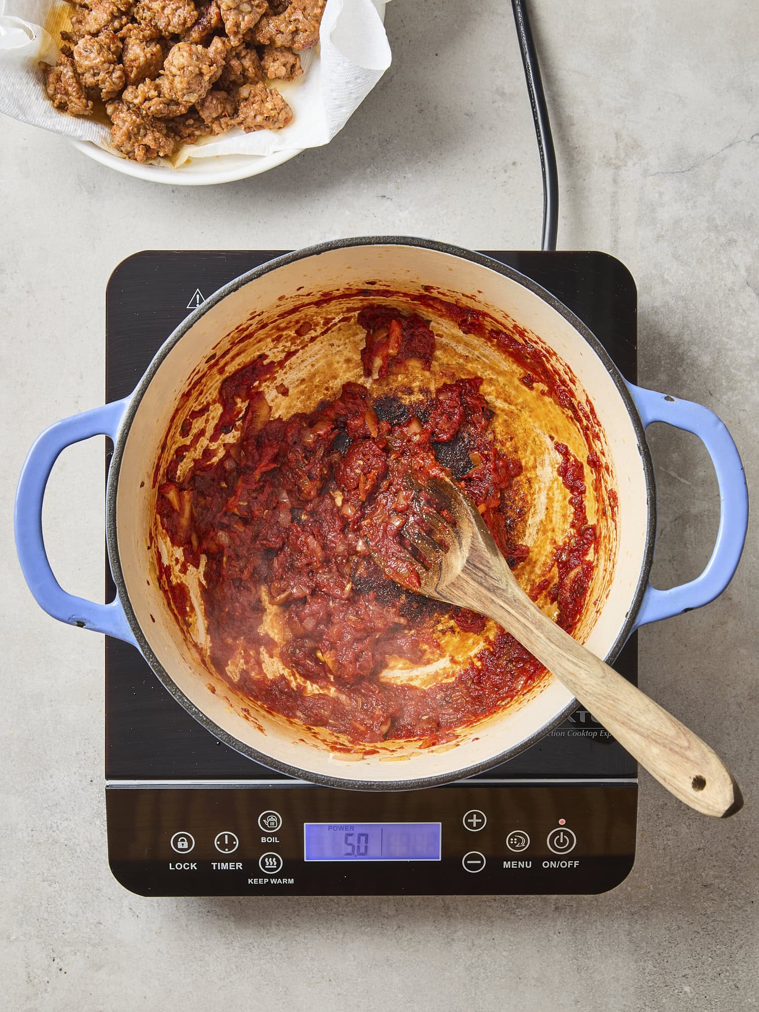 Tomato paste being stirred into a pot with onions and spices.