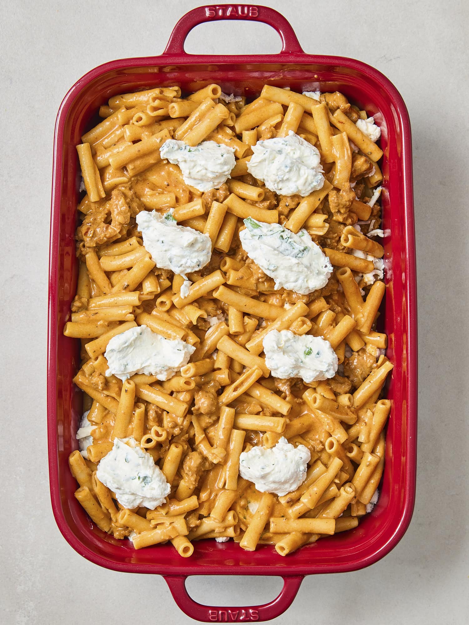Red baking dish with dollops of ricotta mixture on pasta.