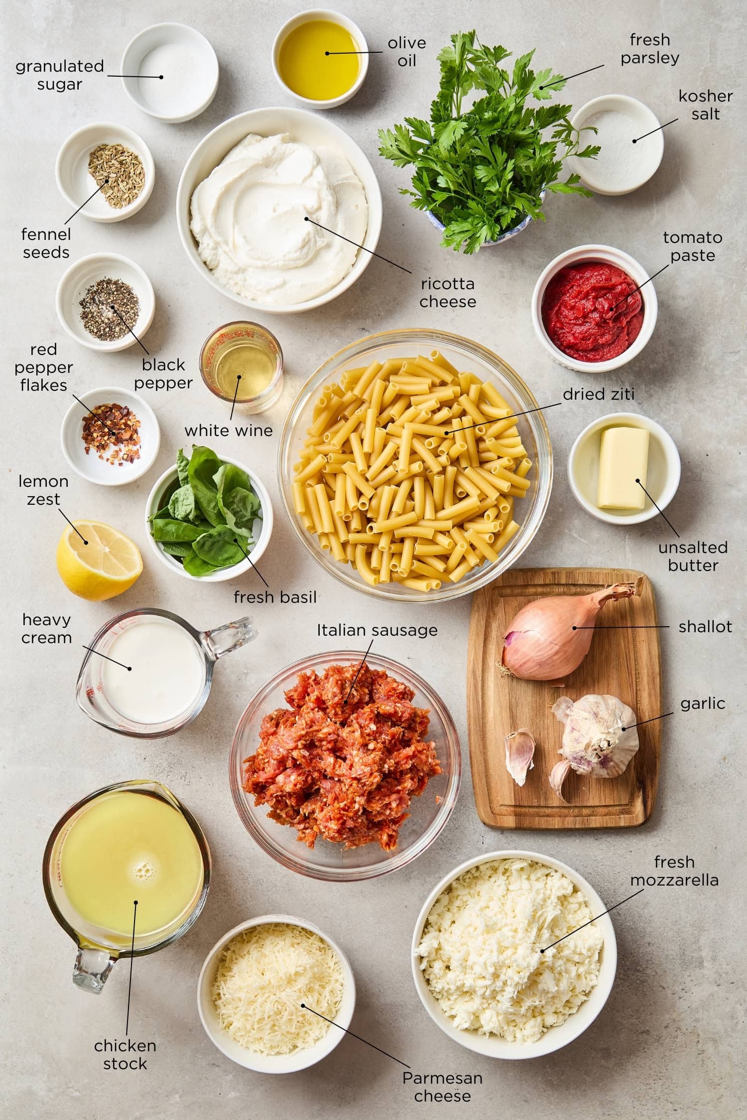 Concrete surface with ingredients needed for a baked ziti including pasta, tomato paste, cream, and more.