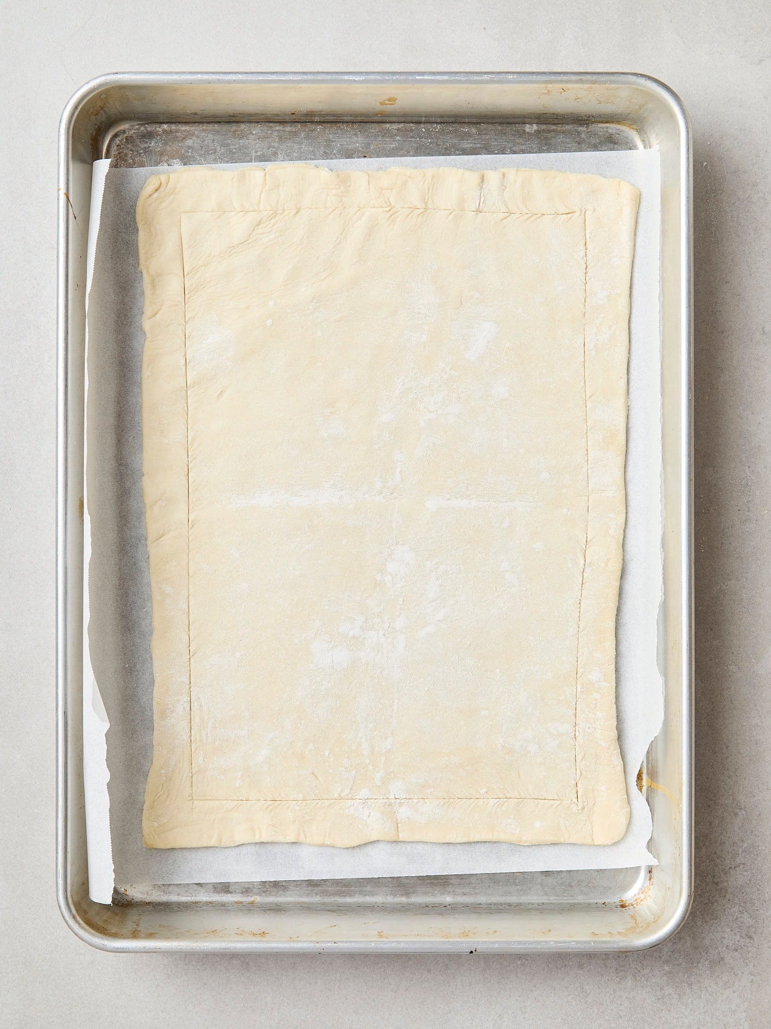Baking sheet with piece of puff pastry scored around the edges.