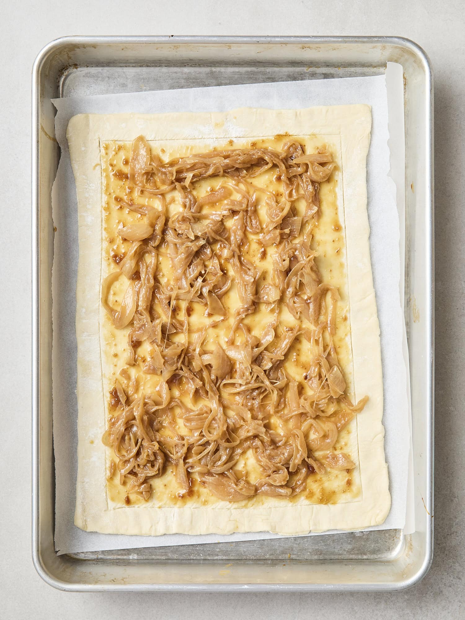 Piece of puff pastry with scored edges and mustard mixture and caramelized onions.