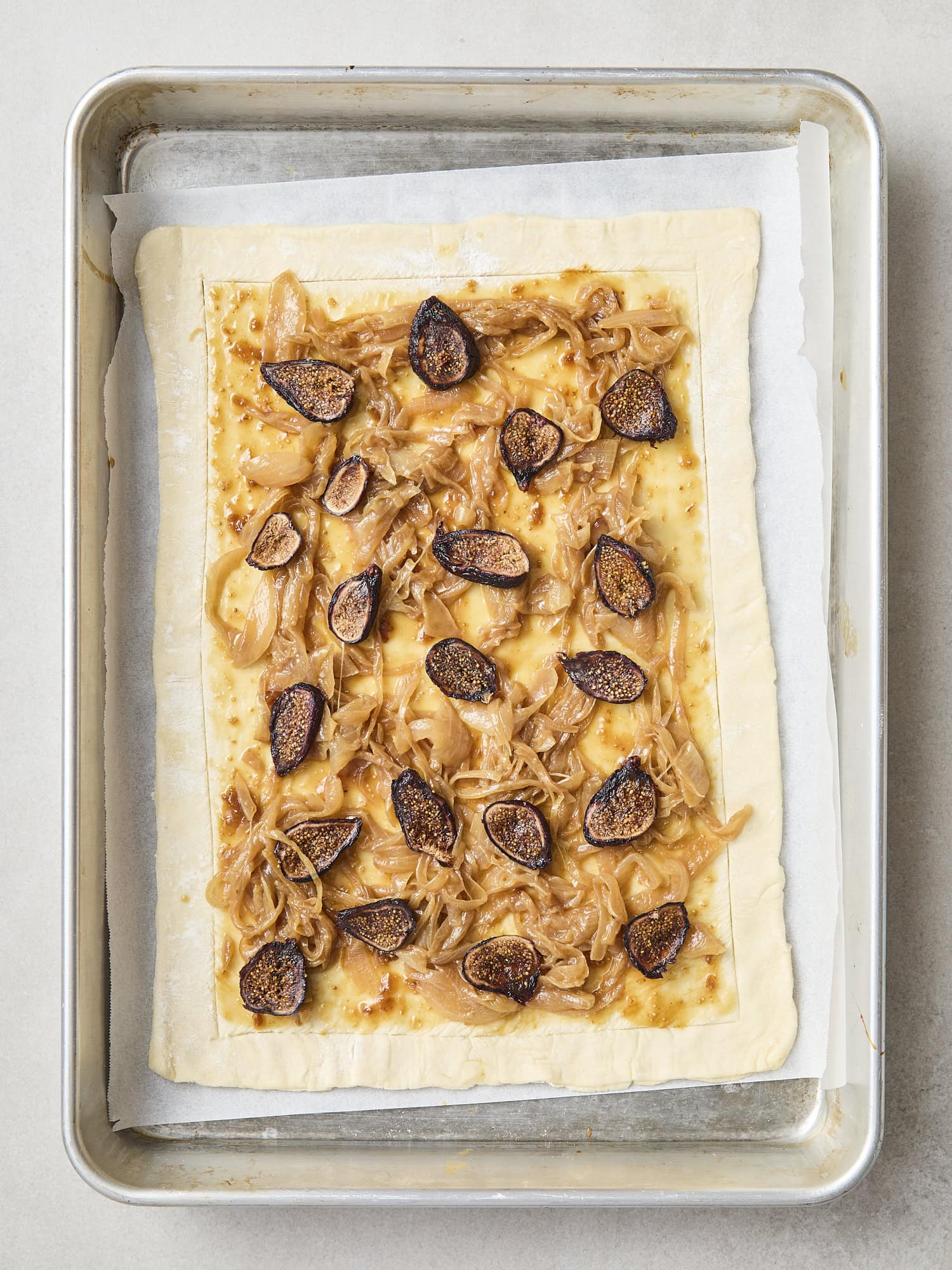 Piece of puff pastry with sliced figs on top of caramelized onions.