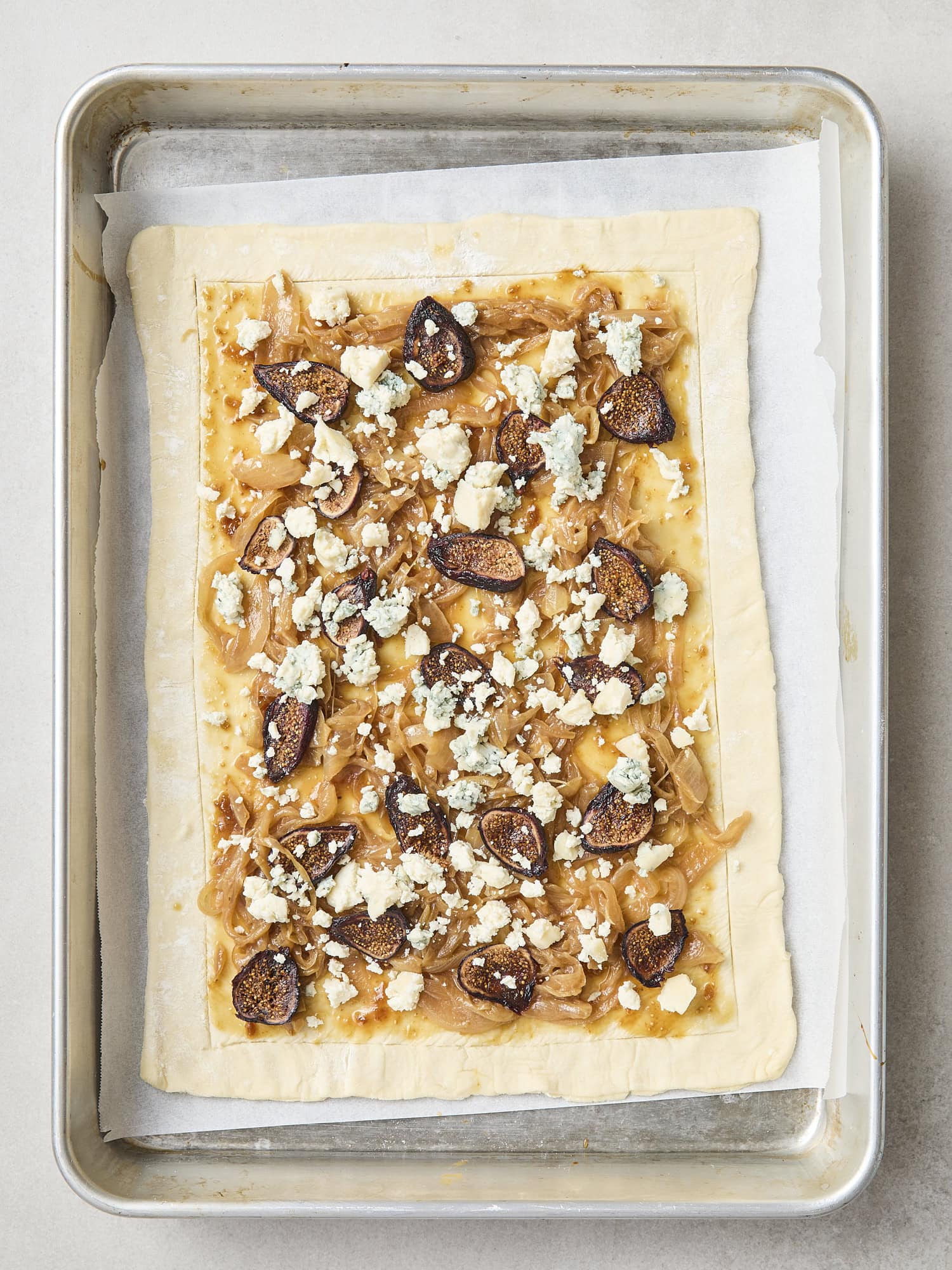 Blue cheese sprinkled on top of figs with caramelized onions on piece of puff pastry.