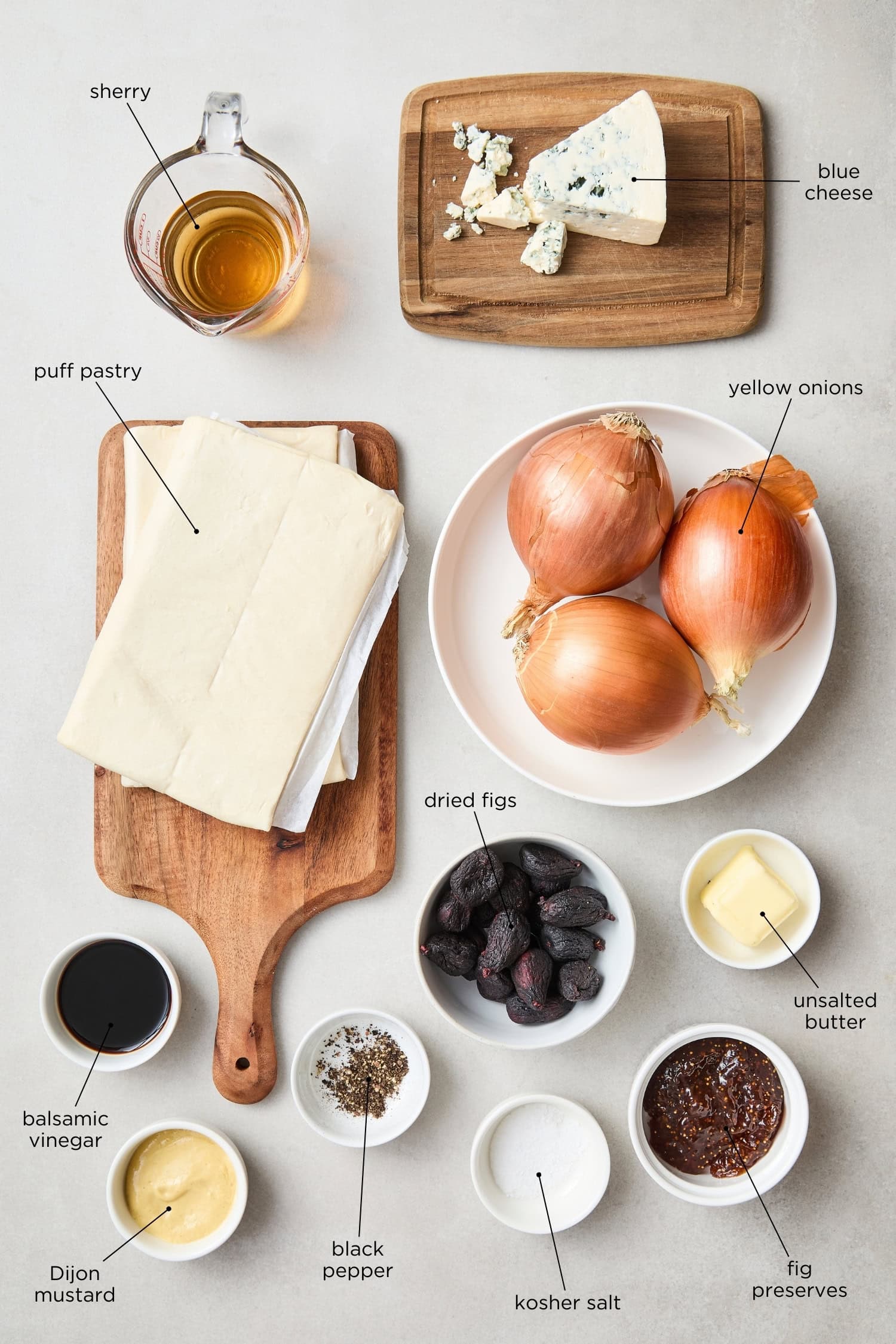 Concrete surface with ingredients needed for a caramelized onion tart including figs, puff pastry, and more.