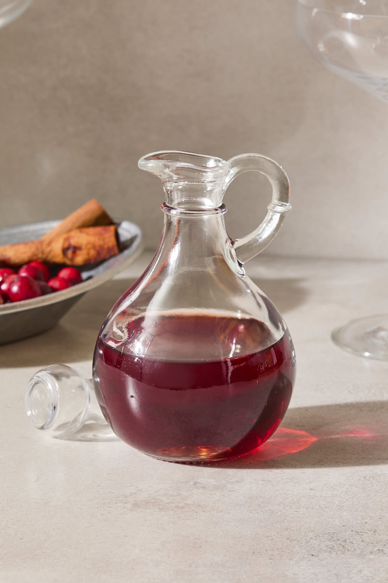 Glass bottle filled with cranberry simple syrup with cinnamon sticks and cranberries in background.