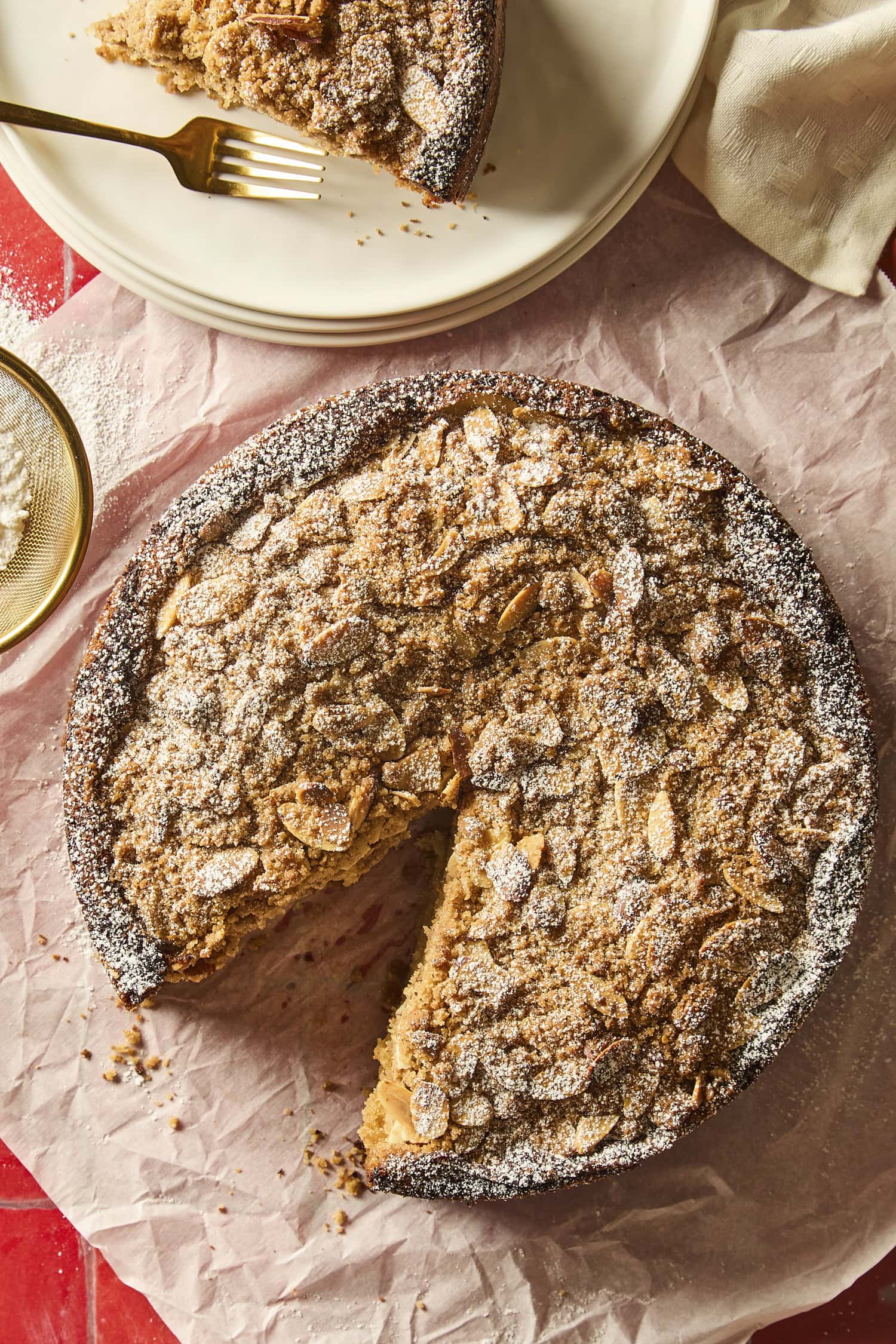 Coffee cake dusted with powdered sugar with sliced almond streusel on top and slice removed.
