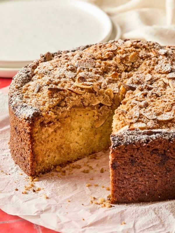 Slice taken out of a frangipane coffee cake with almond streusel topping with plates in background.