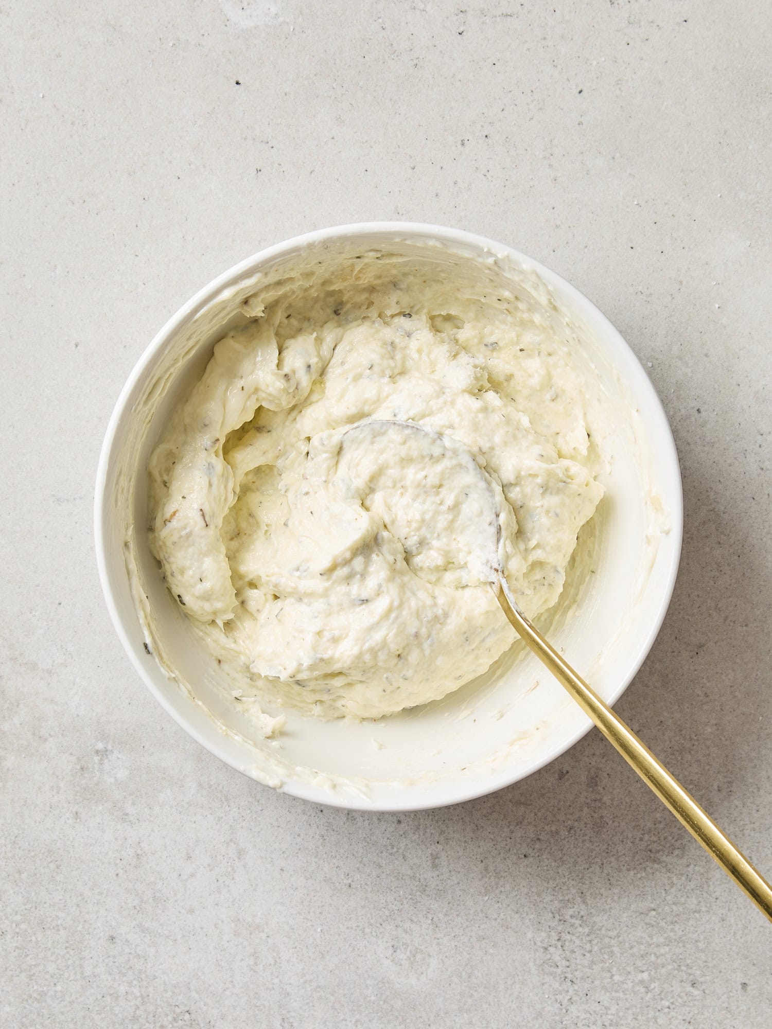 White bowl filled with mayonnaise, butter, and garlic additions to create a spread.