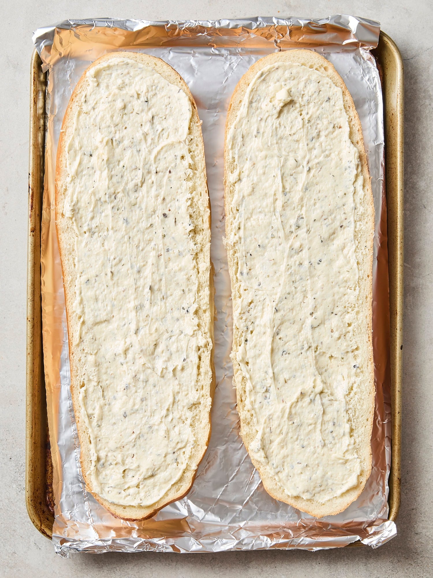 Two pieces of Italian bread spread with mayonnaise and butter mixture for garlic bread.