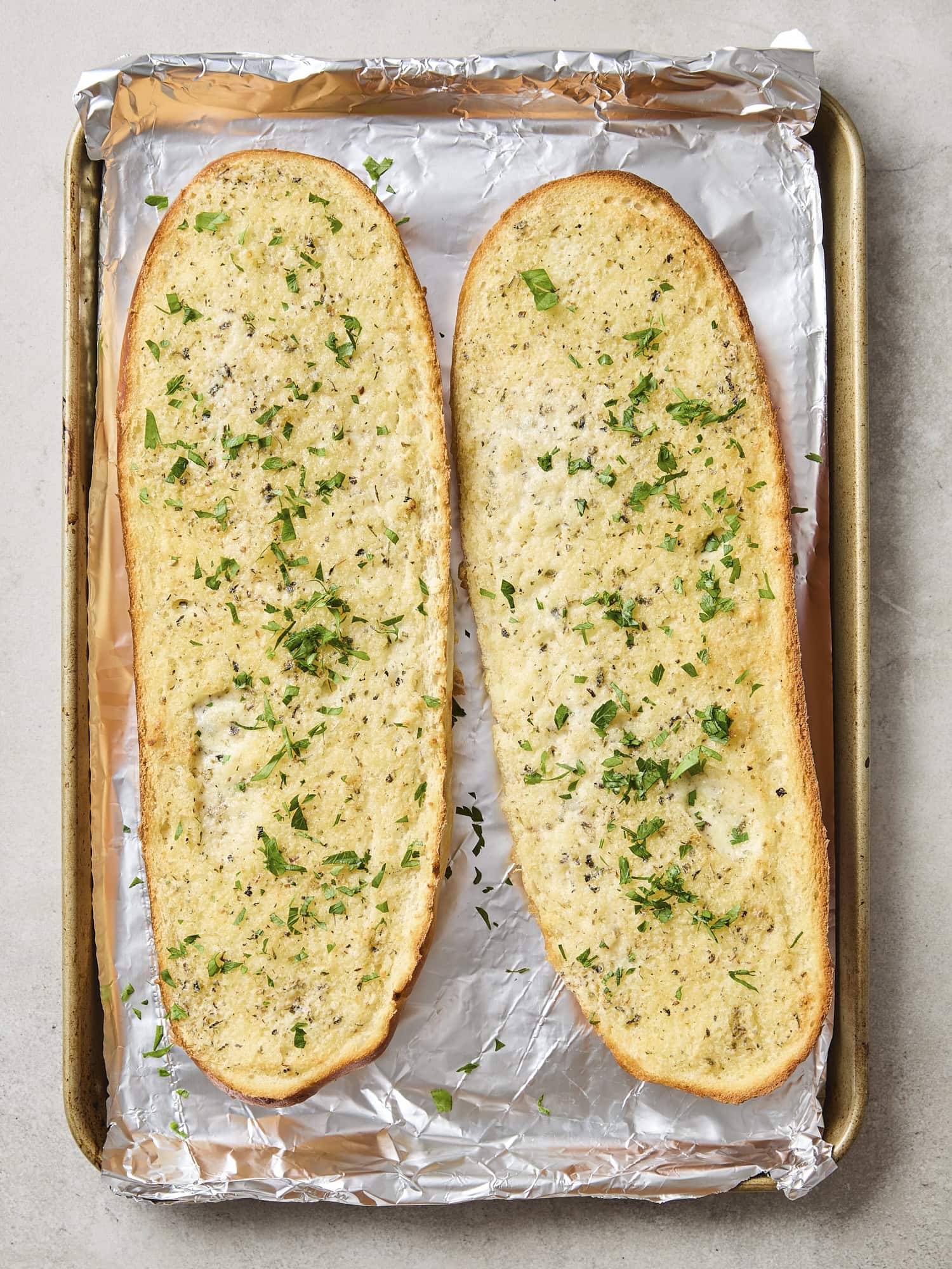 Two halves of garlic bread sprinkled with parsley after being baked.