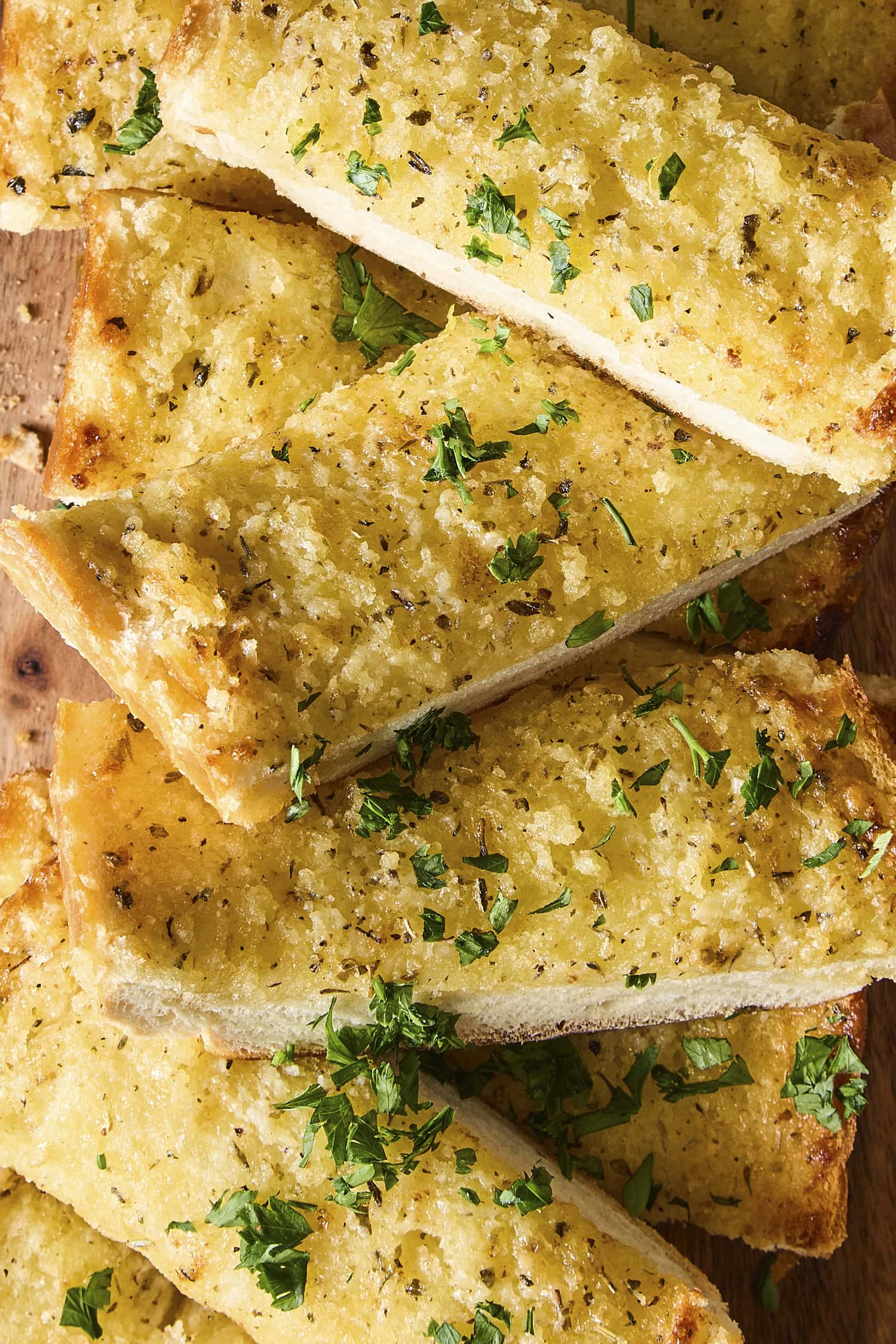 Slices of garlic bread with parsley sprinkled on top laying on top of each other.