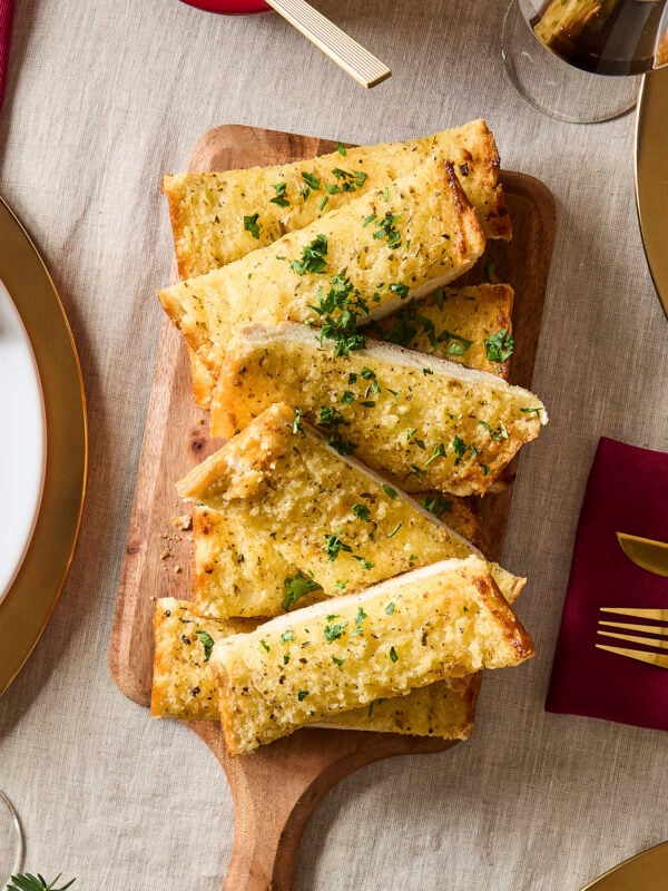 Cutting board filled with slices of garlic bread with fresh parsley on top.