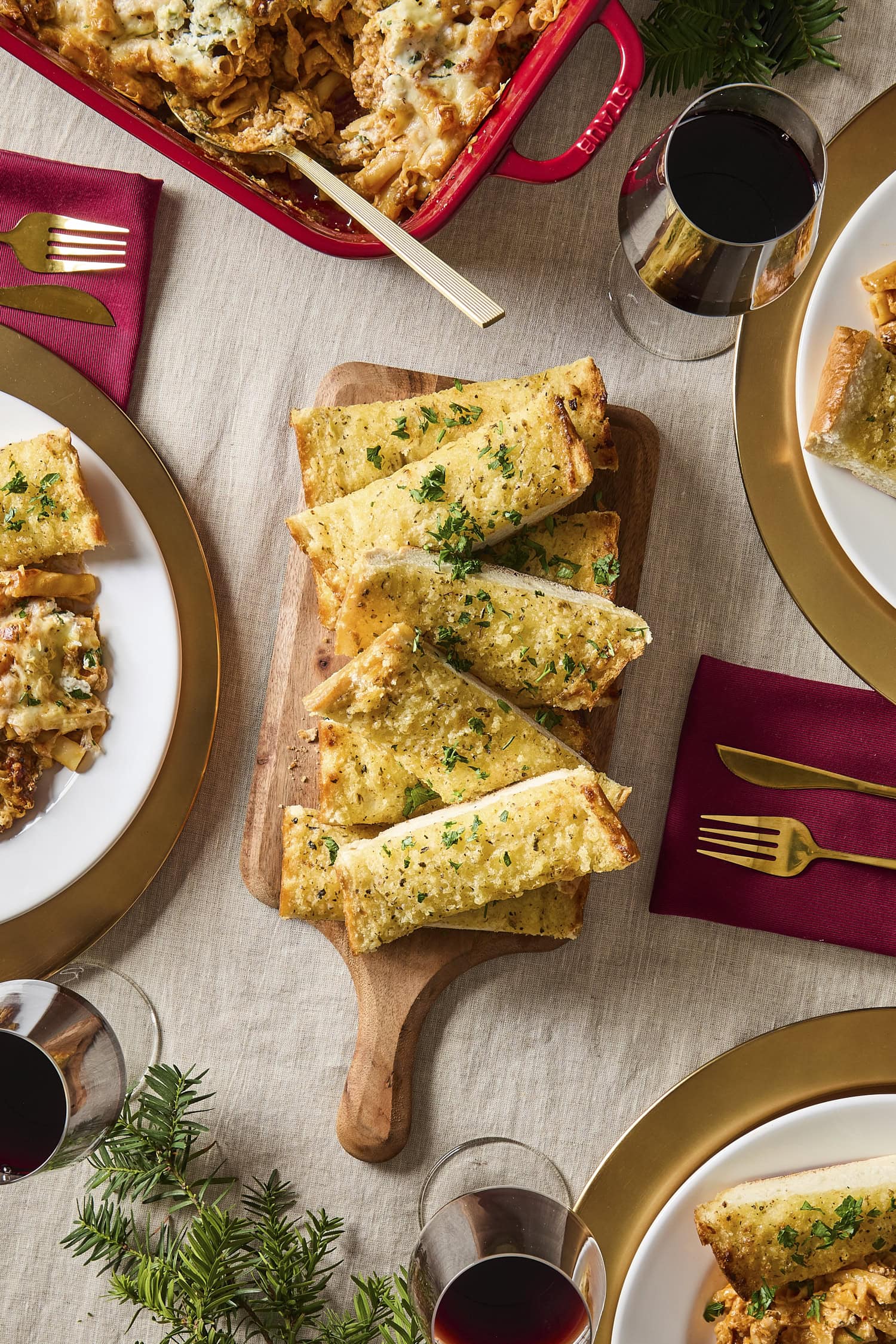 Board with slices of garlic bread with plates and silverware all around.