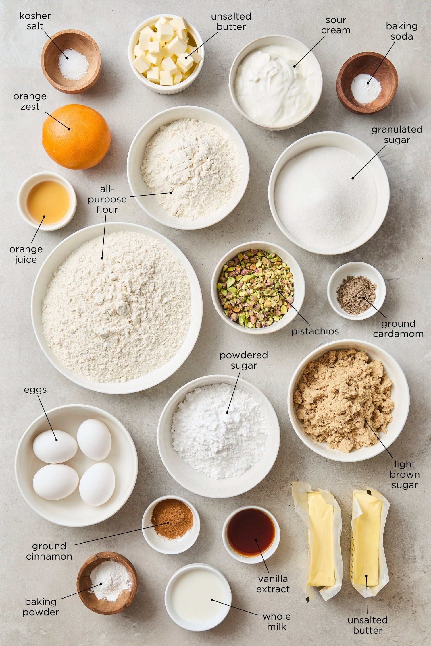 Concrete surface filled with ingredients needed for pistachio muffins including flour, eggs, butter, sugar, pistachios, and more.
